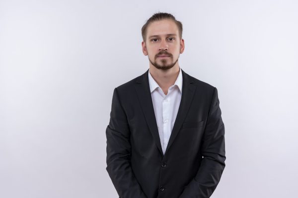 handsome business man wearing suit loking at camera with serious expression standing over white background