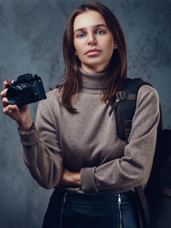 brunette-female-traveler-with-backpack-holds-compact-photo-camera